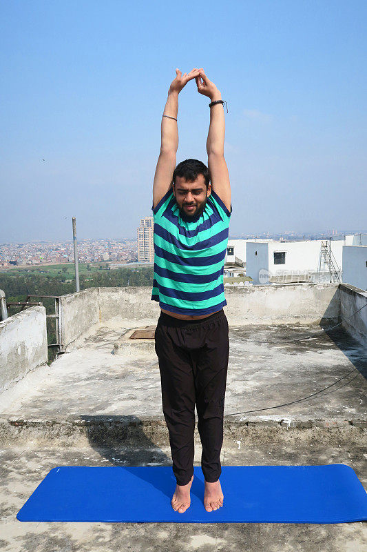 印度男子在屋顶上练习站立敬礼(Urdhva Hastasana)瑜伽姿势，德里，印度